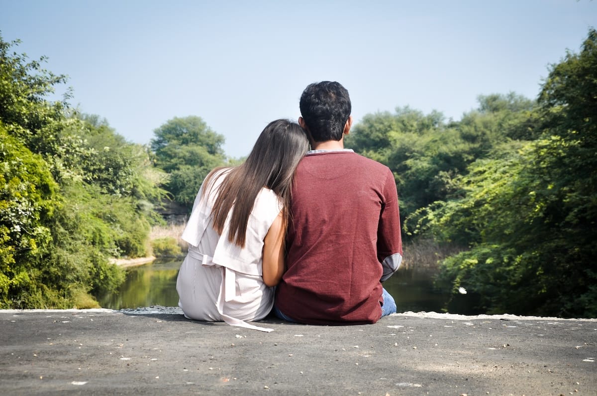 A couple sitting close together by a lake, seen from behind
