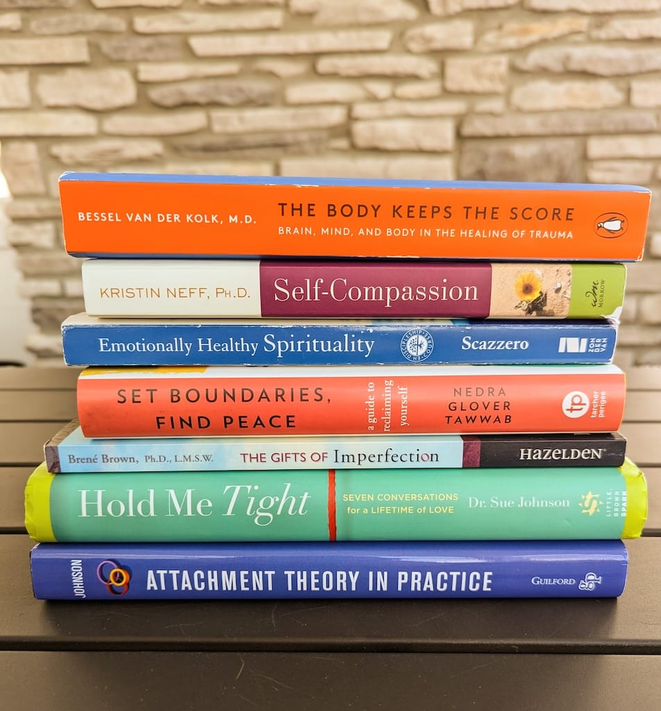 A stack of books on relationships and healing, including Hold Me Tight and The Body Keeps the Score
