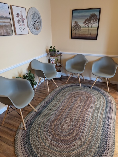 Waiting area with four chairs and a colorful rug where clients can wait for their therapy appointments.